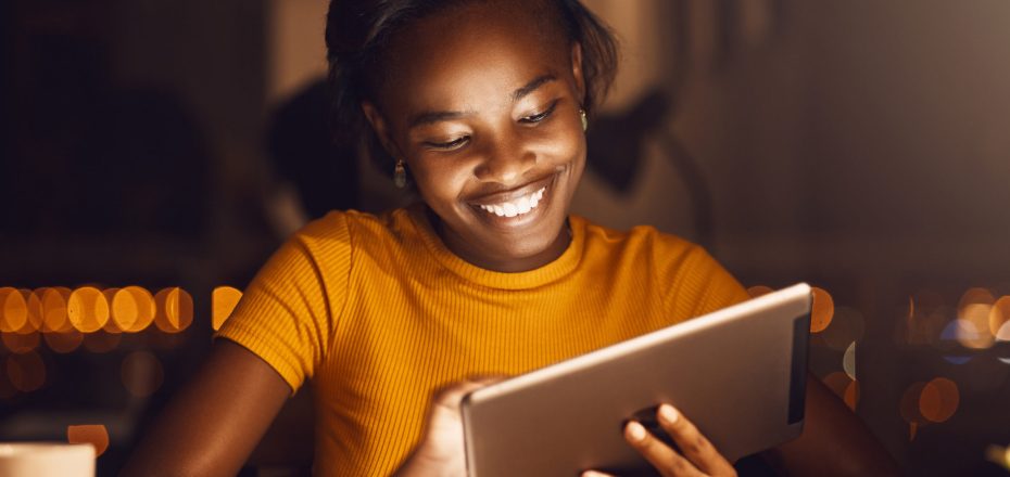 Beautiful, happy and smiling female student using a tablet to browse the internet, do research or scroll on social media while working at home. Cheerful, young and joyful girl searching the web.