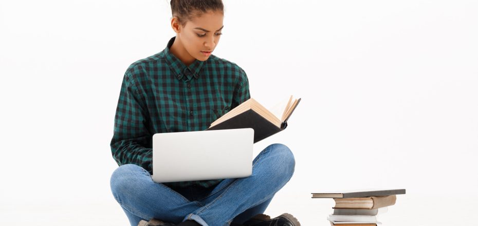 Portrait of young beautiful african girl with laptop and books reading over white background. Copy space.